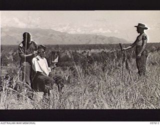 KAIAPIT, NEW GUINEA. 1943-09-26. NX127106 LIEUTENANT D. C. MCRAE OF THE 2/27TH AUSTRALIAN INFANTRY BATTALION CUTTING THE HAIR OF NX129110 PRIVATE F. BAKER WHILE SX12357 PRIVATE N. CHAPMAN STANDS ..