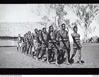 BISIATABU, NEW GUINEA. 1943-07-01. NEW GUINEA NATIVE RECRUITS OF THE 1ST PAPUAN INFANTRY BATTALION TRAINING COMPANY DRILLING WITH CORPORAL IN CHARGE, CORPORAL DAERA, AT REAR OF THE SQUAD, IN WHITE ..