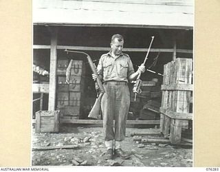 LAE, NEW GUINEA. 1944-09-27. A STAFF SERGEANT OF THE 43RD FIELD ORDNANCE DEPOT SHOWING TWO VERY BADLY DAMAGED .303 LEE ENFIELD RIFLES WHICH HAVE BEEN RETURNED TO STORE