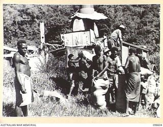 BULOLO, NEW GUINEA. 1945-10-17. NATIVES SEWING UP BAGS IN FRONT OF THE WAU POWER STATION. THIS POWER STATION WAS WRECKED DURING THE WAU CAMPAIGN IN ACCORDANCE WITH THE SCORCHED EARTH POLICY. THE ..