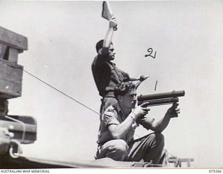 MADANG, NEW GUINEA. 1944-08-18. NX99720 SAPPER H. AULD (USING LAMP) (1) SX28255 PRIVATE C.H. RICHARDSON (USING FLAGS) (2) BOTH MEMBERS OF THE 12TH SMALL SHIPS COMPANY, SIGNALLING THE 2/11TH GENERAL ..