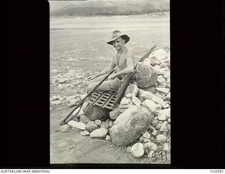 VIVIGANI, GOODENOUGH ISLAND, PAPUA. C. 1944. LEADING AIRCRAFTMAN F. H. EDELSTEN, WARRNAMBOOL, VIC, RESTS ON HIS PARK BENCH MADE OF PSP (PIERCED STEEL PLATING, USED TO SURFACE AIRSTRIPS) IN BETWEEN ..