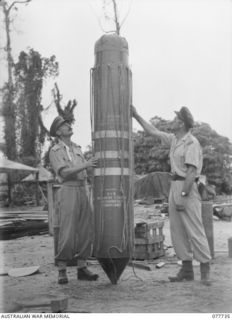 BOUGAINVILLE ISLAND. 1944-12-25. OFFICERS OF THE AUSTRALIAN MILITAURY FORCES AND THE RAAF GIVING A FINAL CHECK TO A "STOREPEDO" CONTAINING AN AUSTER AIRCRAFT PROPELLER WHICH IS TO BE DROPPED BY A ..