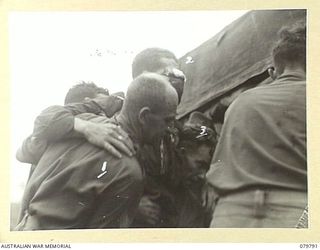 BUT AREA, NEW GUINEA. 1945-03-17. NX32941 PRIVATE J.J. PARKES, NO.10 PLATOON, B COMPANY, 2/2ND INFANTRY BATTALION (2), WHO HAD BEEN SHOT THROUGH THE FACE, RECEIVES ASSISTANCE FROM NX15264 SERGEANT ..