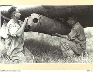 GUSAP, RAMU VALLEY, NEW GUINEA. 1944-01-02. GROUND CREW MEMBERS OF NO. 4 (TACTICAL RECONNAISSANCE) SQUADRON OF THE ROYAL AUSTRALIAN AIR FORCE ATTACHING CONTAINERS TO THE BOMB RACKS ON A WIRRAWAY. ..