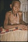 Weaving: Bomtavau, her head shaved in mourning, displays long skirt made of banana leaf fibers