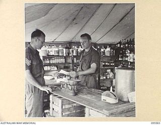 CAPE WOM, WEWAK AREA, NEW GUINEA. 1945-08-28. SERGEANT A. PINSON, 104 CASUALTY CLEARING STATION HANDING OVER AN ORDER FOR SUPPLIES TO PRIVATE L. BENNETTS, THE DISPENSER