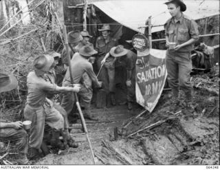 "Johno's Jungle Joint", the Salvation Army Red Shield hut on Shaggy Ridge showing troops of the 2/9th Infantry Battalion receiving a welcome cup of coffee.  Identified on right is NX150554 Private ..