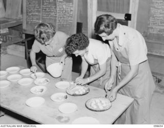 LAE, NEW GUINEA. 1945-11-08. LANCE CORPORAL R. SOLOMON (1), SERGEANT J. HARVEY (2) AND SERGEANT M. BRETT (3), SERVING APPLE PIE DURING THE COOKERY AND HOME CRAFT COURSE HELD AT "LAEWAS" COLLEGE