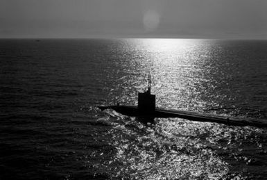 A silhouetted port quarter view of a nuclear-powered submarine underway