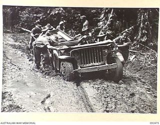 BOUGAINVILLE. 1945-05-20. MEMBERS OF 3 SURVEY BATTERY, ROYAL AUSTRALIAN ARTILLERY, PUSHING A JEEP AND TRAILER LOADED WITH EQUIPMENT THROUGH A MUDDY SECTION OF THE BUIN ROAD NEAR THE HONGORAI RIVER