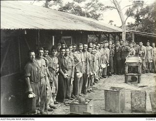 KIRIWINA, TROBRIAND ISLANDS, PAPUA. 1943-11-12. AIRMEN OF NO. 76 (KITTYHAWK) SQUADRON RAAF LINE UP OUTSIDE THE MESS FOR LUNCH WITH THEIR MESS KIT OF CUP, PLATE, KNIFE AND FORK