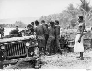 SIALUM BEACH, NEW GUINEA. 1944-01-08. NATIVES LOADING 44 GALLON DRUMS OF PETROL AND OIL ONTO A JEEP