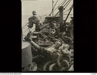 AT SEA BETWEEN GOODENOUGH ISLAND AND THE TROBRIAND ISLANDS, PAPUA. 1943-11-27. LEADING AIRCRAFTMAN (LAC) C. W. MILLINGTON OF ALBURY, NSW, WITH FOOT UP ON DEPTH CHARGE TALKING TO LAC E. A. TIPPERTON ..