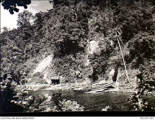 Rabaul, New Britain, 1945-10. Japanese barges lie hauled up on the shore of a quiet bay, near the entrance to a tunnel (left) where the Japanese formerly hid their barges from view. The tunnel has ..