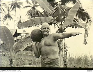 MADANG, NEW GUINEA. C. 1944. 272783 SQUADRON LEADER J. P. HIGGINS, BRISBANE, QLD, KEEPS IN TRIM AT A FORWARD RAAF BASE IN NEW GUINEA BY THROWING A HEAVY MEDICINE BALL