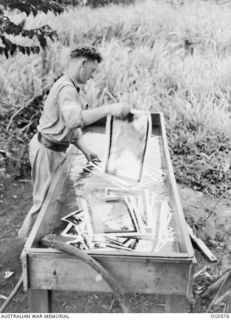 MILNE BAY, PAPUA. 1943-07-31. A CORPORAL PHOTOGRAPHER IS WASHING PRINTS WHICH ARE DRIED AND STUCK TOGETHER AS MOSAICS AND THEN PHOTOGRAPHED. THE PRINTS WERE OBTAINED FROM FILM EXPOSED DURING AN ..