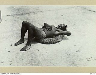 MILNE BAY, PAPUA, NEW GUINEA. 1944-04-03. A NATIVE RESTING ON AN OLD MOTOR TYRE AT THE 2ND BULK PETROLEUM STORAGE COMPANY. THE TYRES ARE USED TO PREVENT DAMAGE TO DRUMS DURING UNLOADING