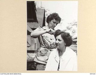 LAE, NEW GUINEA. 1945-05-08. CORPORAL O. TAYLOR (1), A HAIRDRESSER IN CIVILIAN LIFE, TRIMS THE HAIR OF CORPORAL E.C. NELSON (2), SHORTLY AFTER THEIR ARRIVAL AT THE NEWLY CONSTRUCTED AWAS BARRACKS ..