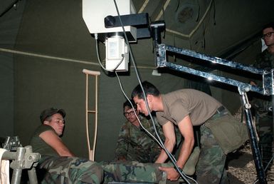 SPC5 Eric L. Zamora, a medic with the 25th Inf. Div., prepares to x-ray the leg of PVT Felix Gonzalez during an exercise at the Pohakuloa Training Area. Looking on is CPT Leif G. Johnson, commander of Company C