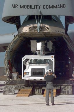 A C-5 Galaxy crew member out of Travis Air Force Base, California, marshals a power truck from a C-5 Galaxy aircraft as it arrives at Andersen Air Force Base, Guam, to deliver power trucks from Hawaii. The trucks will aid the Guam Power Authority in restoring power to the island after Typhoon Paka