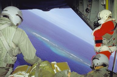 Santa Claus (SSGT Ernest A. Allen) and another airman look down from the cargo bay of their C-130 Hercules aircraft, which is delivering donated Christmas gifts by parachute onto local islands. The presents were collected by volunteers from the 43rd Security Police Squadron, the 605th Military Airlift Support Squadron, and the 43rd Munitions Maintenance Squadron