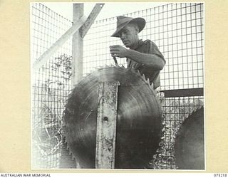 LAE, NEW GUINEA. 1944-08-06. QX19131 LIEUTENANT E.J. BATES, SECTION LEADER, 2/3RD FORESTRY UNIT FILING THE TEETH OF A LARGE CIRCULAR SAW IN THE UNIT WORKSHOPS