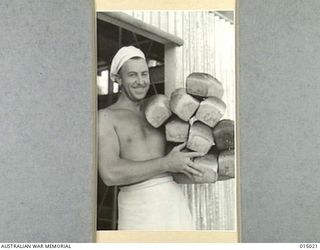 1943-06-15. NEW GUINEA. A.I.F. BAKERS AT WORK IN NEW GUINEA. PTE. N. BLACKSHAW OF WEST RYDE, N.S.W. WITH AN ARMFUL OF LOAVES. (NEGATIVE BY N. BROWN)