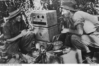 Sergeant Frank J Parmiter of Coburg, Vic, and Corporal Ivan G Pritchard, of Kensington, NSW, spotters with the New Guinea Air Warning Wireless Company (NGAWW), at work beside their AWA radio at an ..