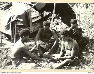 KELANOA, NEW GUINEA. 1944-03-04. MEMBERS OF "A" COMPANY, 1ST PAPUAN INFANTRY BATTALION, PLAYING CARDS OUTSIDE THEIR "DOOVER", A SHELTER MADE FROM BAMBOO, TARPAULINS AND PALM LEAVES. "A" COMPANY, ..