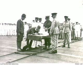 NEW BRITAIN, 1945-09-06. GENERAL HITOSHI IMAMURA, COMMANDER JAPANESE EIGHTH AREA ARMY, SIGNS THE INSTRUMENT OF SURRENDER ON BOARD HMS GLORY OFF RABAUL. (RNZAF OFFICIAL PHOTOGRAPH.)