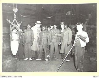 MARIBYRNONG, AUSTRALIA. 1942-10-12. A PARTY OF SIX NEW GUINEA NATIVE SOLDIERS ON A TOUR OF INSPECTION OF THE MUNITION WORKS WATCH A LARGE SHELL BEING FILLED WITH EXPLOSIVE