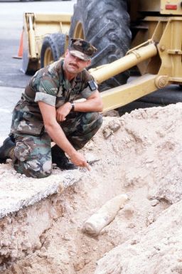 A member of the Guam Detachment of Explosive Ordnance Disposal Mobile Unit 5, points to a projectile uncovered during digging at a construction site. The Guam Police Department called in the unit to inspect the projectile, a 5-inch Japanese live round remaining from World War II