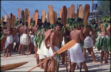 Groups of men in white lava lava holding wooden paddles