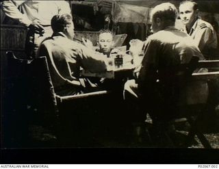 Tadji, New Guinea. c. 1944. The crew of Department of Aircraft Production (DAP) Beaufort bomber A9-557, 100 Squadron RAAF, playing a game of cards in at night. Left to right: unknown (part ..