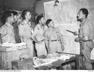 RAMU VALLEY, NEW GUINEA. 1944-01-02. THE AIR LIAISON OFFICER OF NO. 45 AIR LIAISON SECTION, VX20171 LIEUTENANT J. FETHERSTON-HAUGH (1) STUDYING A MAP OF THE RAMU VALLEY AREA WITH PILOTS OF "A" ..