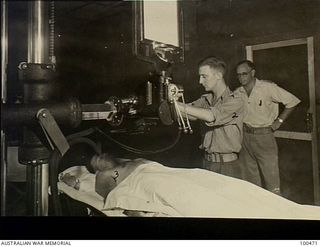 Port Moresby, New Guinea. 1944-05-29. Captain S. U. Sherrett (right) supervising Staff Sergeant Evans as he x-rays patient Private H. N. Warner at 2/1st Australian General Hospital