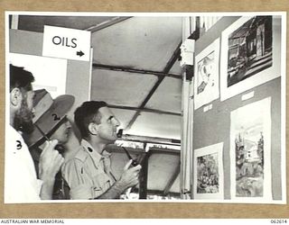 PORT MORESBY, PAPUA, NEW GUINEA. 1943-12-23. PERSONNEL EXAMINING THE PRIZE WINNING WATER COLOURS AT THE ARTS AND CRAFTS EXHIBITION STAGED BY THE AUSTRALIAN ARMY EDUCATION SERVICE, HEADQUARTERS, ..