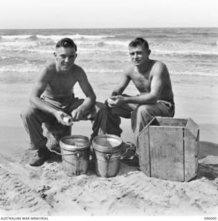 WEST WEWAK BEACH, NEW GUINEA. 1945-09-01. PRIVATE R.C. BARBERA (1) AND PRIVATE N.G. SMITH (2), MEMBERS OF 2/11 INFANTRY BATTALION PEELING POTATOES ON THE BEACH. THE UNIT LINES ARE BESIDE THE BEACH