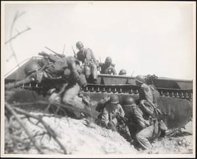 Marines in this wave leap from their amphibious tractor for the shelter of the sand dunes