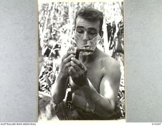 1943-01-27. PAPUA. SANANANDA AREA. SGT. R. HEINITZ OF MONTANA USES HIS HIGHLY POLISHED KNIFE AS A MIRROR. (NEGATIVE BY BOTTOMLEY)