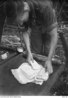 KIARIVU, NEW GUINEA, 1945-08-10. SERGEANT S. FYFE, 2/7 INFANTRY BATTALION WRAPPING CAPTURED JAPANESE DOCUMENTS FOR DISPATCH TO BASE FOR DECIPHERING. THESE DOCUMENTS WERE CAPTURED WHEN A JAPANESE ..