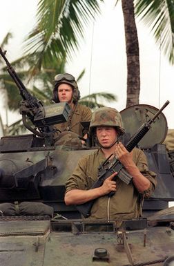 A front view medium close up of US Marine Corps Lance Corporal (LCPL) Ryan Roth armed with a 5.56mm M16A2 assault rifle and Corporal (CPL) Mike Gaffey manning a 7.62mm M240G machine gun standing watch from a Light Armored Vehicle (LAV-25), at Kaneohe Bay Marine Corps Station (MCS), HI. Marines from 11th Marine Expeditionary Unit (MEU) Camp Pendleton, CA conducted training exercises in Hawaii as part of Operation RIMPAC 96