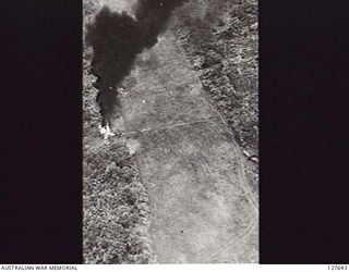 LAE, NEW GUINEA. MALAHANG AIRSTRIP WITH A BURNING "ZEKE" (JAPANESE AIRCRAFT, ZERO) ON ONE SIDE AND TWO MORE ON THE RIGHT IN TREES