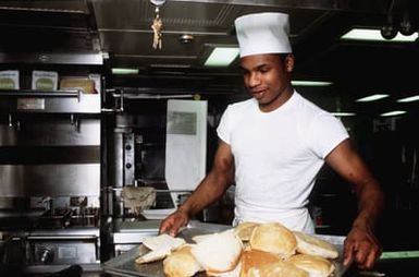 A baker aboard the amphibious assault ship USS GUAM (LPH 9) offers fresh bread during mess. The ship is participating in operations off the coast of Lebanon