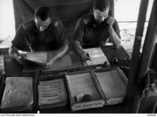 CAPE WOM, NEW GUINEA. 1945-10-17. CAPTAIN W.F. ROBESON, OFFICER- IN- CHARGE DEMOBILIZATION HEADQUARTERS 6 DIVISION (1) AND HIS ASSISTANT LIEUTENANT G.S. RENNIE (2) AT WORK IN THE DEMOBILIZATION ..