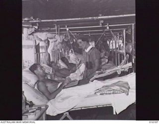 NEW GUINEA. 1943-11-24. AT AN AUSTRALIAN FIELD HOSPITAL AN AUSTRALIAN NURSING SISTER CHATS TO A PATIENT IN A FRACTURE WARD AT THE HOSPITAL