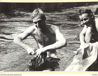 PAPUA, NEW GUINEA. 1942-10. FROM THE CENTRE COURT AT WIMBLEDON TO A CRACK IN THE JUNGLE OF NEW GUINEA CORPORAL J. BROMWICH OF AIR SUPPORT CONTROL SIGNALS SITTING ON A LOG WASHING HIS SHIRT IN A ..