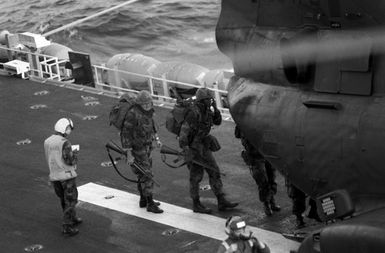 Marines on the flight deck of the amphibious assault ship USS GUAM (LPH 9) prepare to board a CH-46 Sea Knight helicopter during Operation URGENT FURY. They are armed with M16A1 rifles