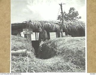 DUMPU, NEW GUINEA. 1944-01-11. VX21014 CORPORAL A. M. GRUMONT AT THE DOORWAY OF THE 7TH DIVISION SIGNALS WIRELESS TELEPHONE RECEIVING HUT
